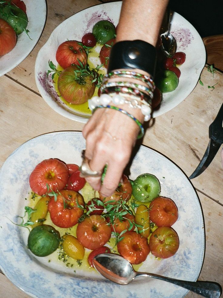 Hands arranging colorful heirloom tomatoes and fresh herbs on a rustic plate